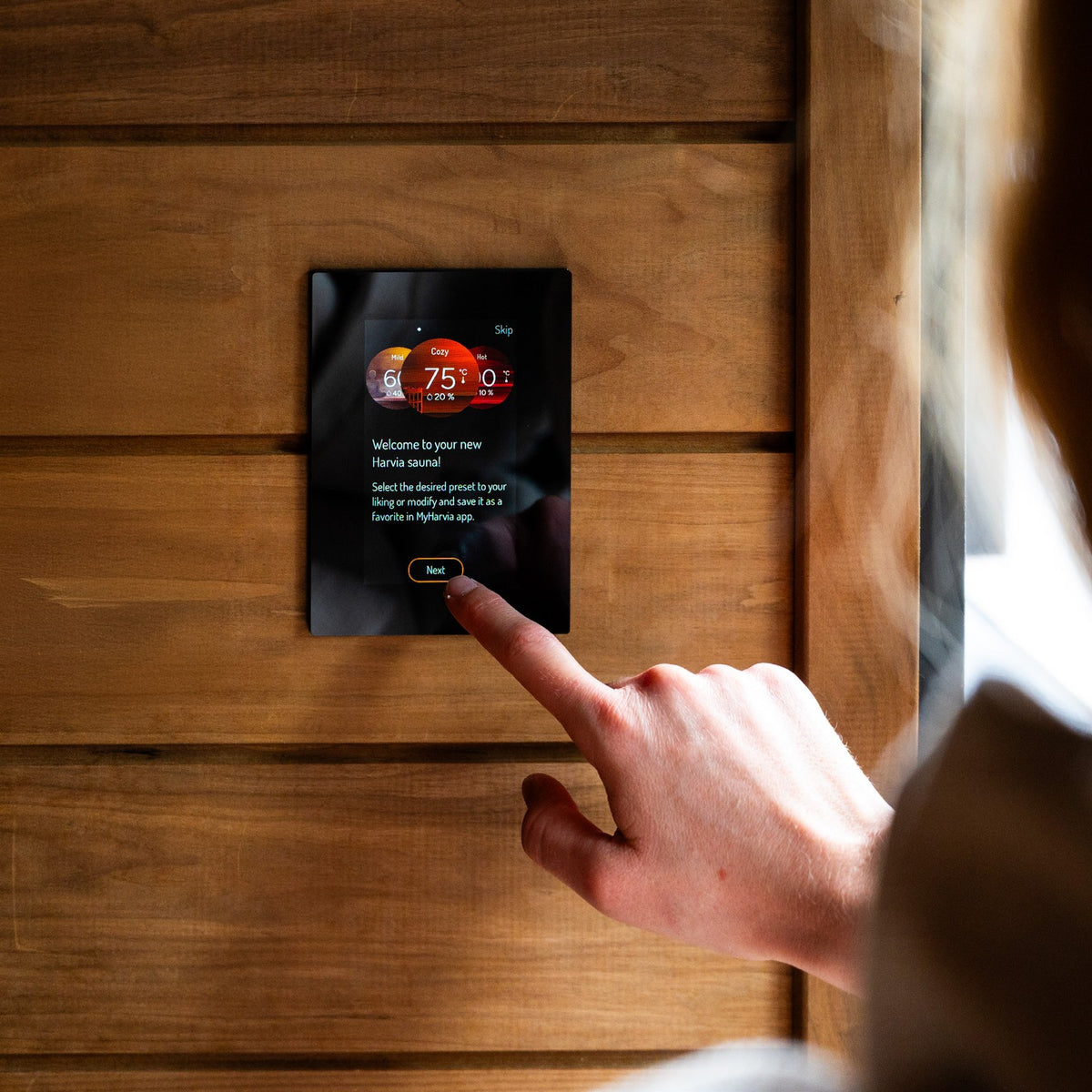 Harvia Fenix control panel surface mounted on a timber sauna wall being operated by hand